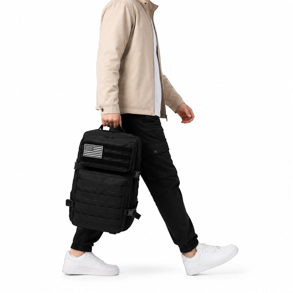 Sac à dos tactique noir Univers Sac en Oxford avec système Molle et patch drapeau, porté à la main par un homme.