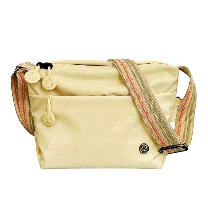 Sac bandoulière Univers Sac beige en nylon et coton bio, léger, avec fermeture éclair et bandoulière rayée.