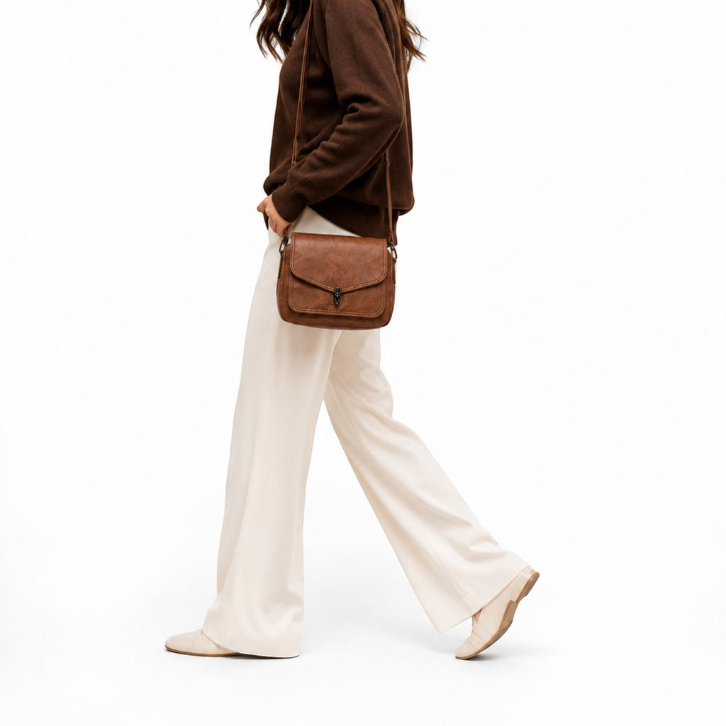 Sac bandoulière vintage en cuir PU marron avec fermeture à rabat et bijouterie argentée, porté par une femme.