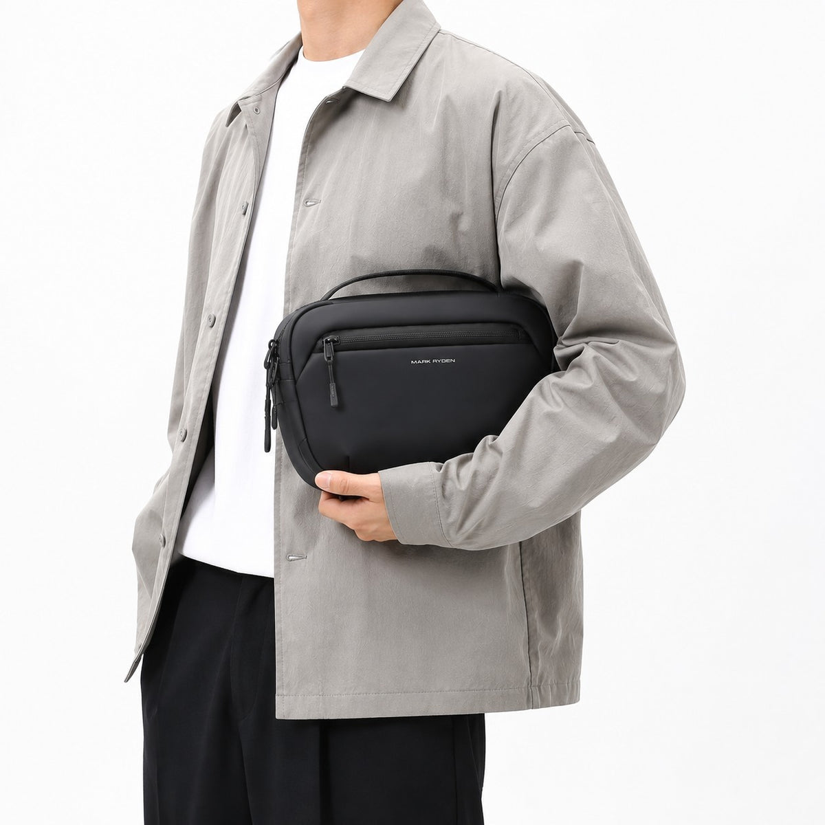 Sac bandoulière noir Mark Ryden pour homme, compact et imperméable, porté à la main sur un fond blanc.