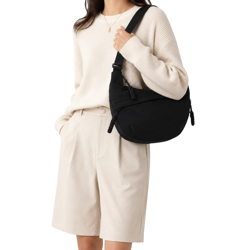 Sac à bandoulière noir en nylon de forme hobo, porté par une femme, avec fermeture éclair et détails tressés.
