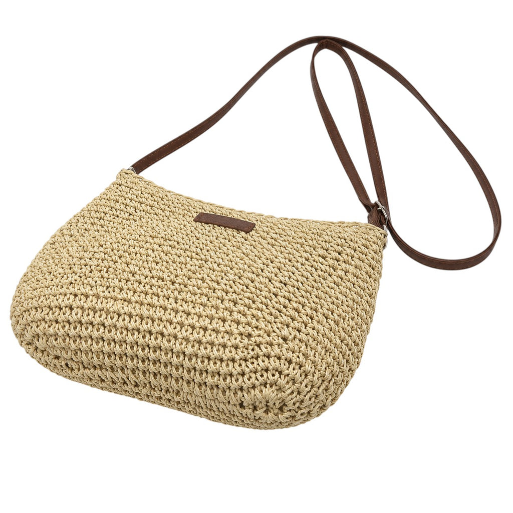 Sac bandoulière beige en paille tressée avec une anse en cuir marron et une petite étiquette de marque. Fermeture zippée.