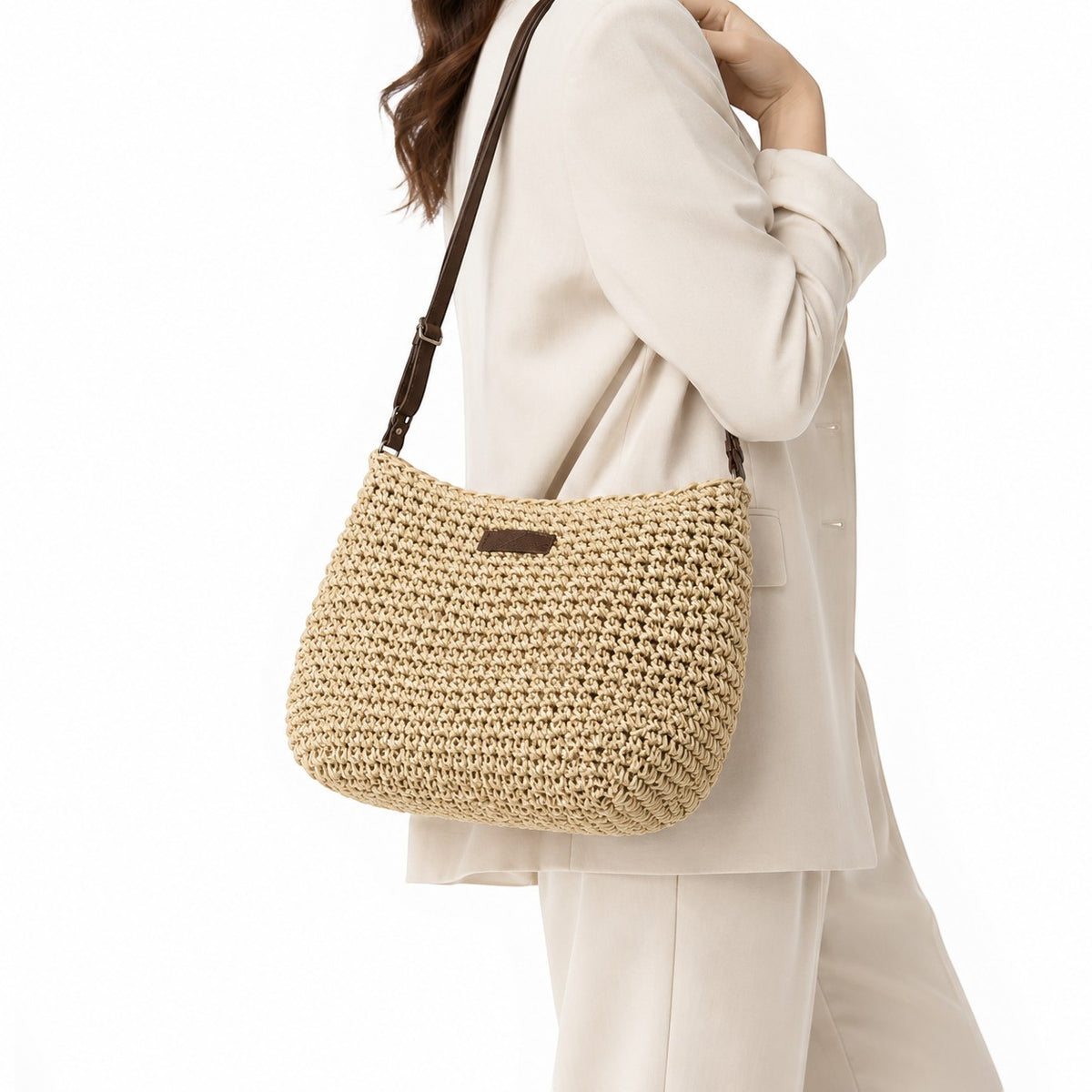 Sac bandoulière beige en paille tressée, porté par une femme, avec une fermeture éclair et une anse en cuir.
