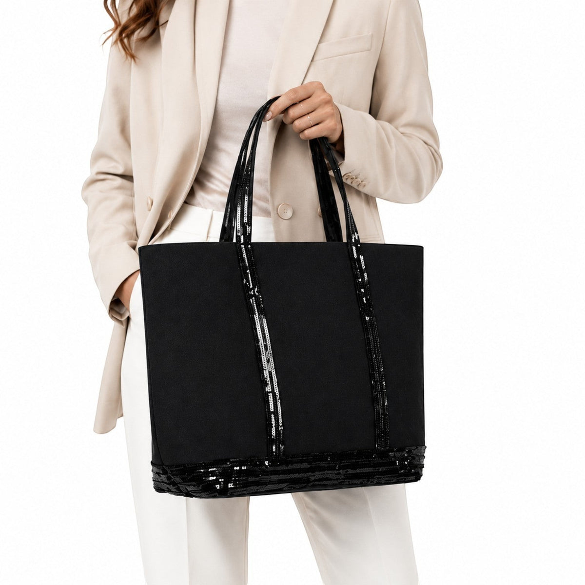 Sac fourre-tout noir en toile avec détails de paillettes brillantes, anses et bordure. Porté par une femme.